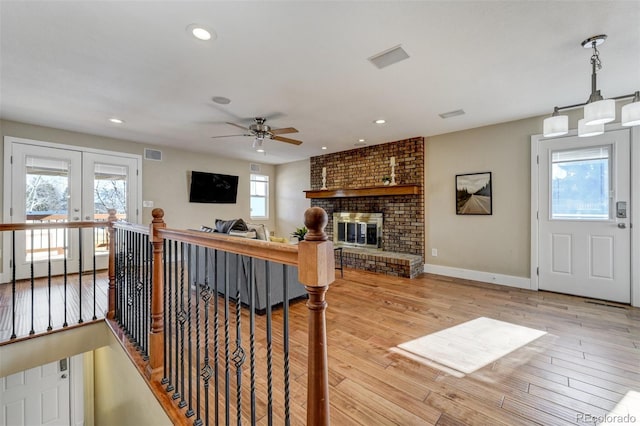 living room with ceiling fan, a brick fireplace, light wood-type flooring, and french doors