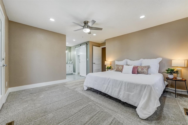 carpeted bedroom with a barn door, connected bathroom, and ceiling fan