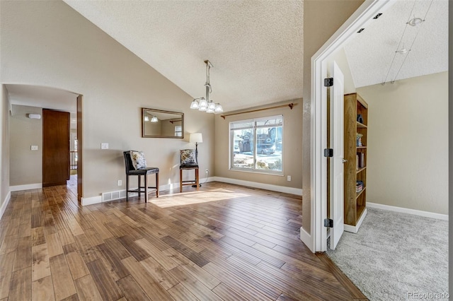 unfurnished dining area featuring hardwood / wood-style flooring, high vaulted ceiling, a textured ceiling, and an inviting chandelier