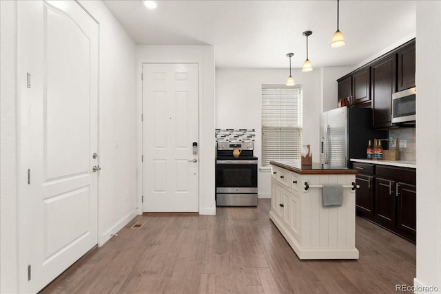 kitchen featuring pendant lighting, stainless steel appliances, decorative backsplash, and wood finished floors