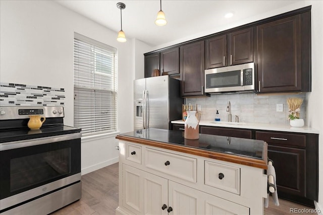 kitchen with dark brown cabinets, a sink, stainless steel appliances, pendant lighting, and backsplash