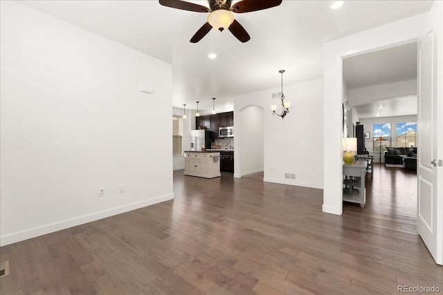 unfurnished living room with ceiling fan with notable chandelier, recessed lighting, dark wood-style flooring, arched walkways, and baseboards