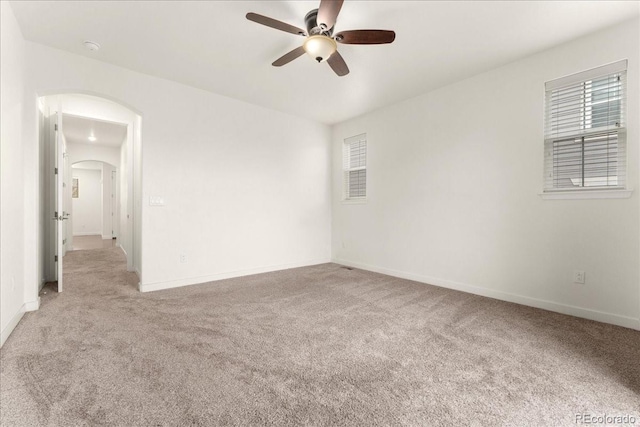 carpeted spare room with a wealth of natural light, arched walkways, a ceiling fan, and baseboards