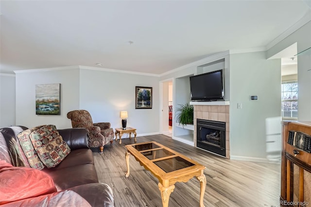 living area featuring baseboards, a tiled fireplace, wood finished floors, and crown molding