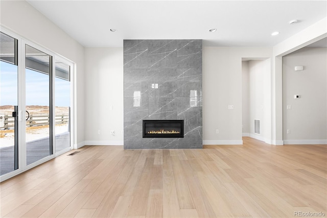 unfurnished living room with visible vents, a high end fireplace, baseboards, light wood-style floors, and recessed lighting