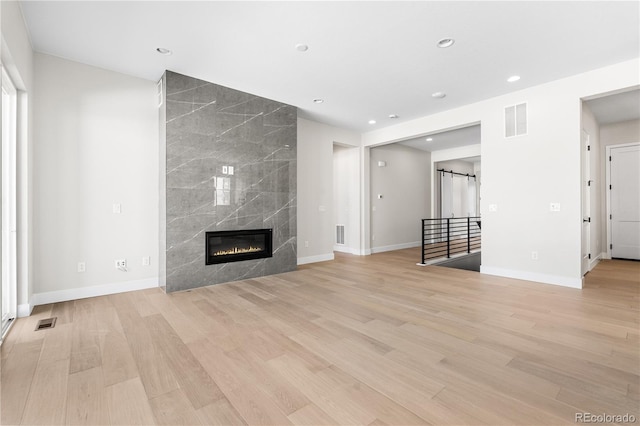 unfurnished living room featuring a high end fireplace, baseboards, light wood-style flooring, and visible vents