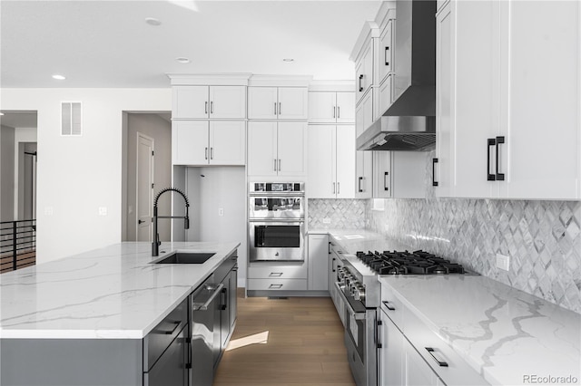 kitchen featuring visible vents, appliances with stainless steel finishes, wood finished floors, a sink, and wall chimney exhaust hood