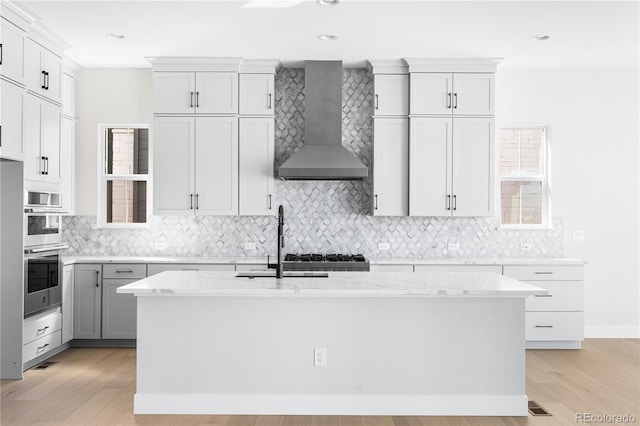 kitchen featuring light wood-style floors, a sink, backsplash, and wall chimney range hood