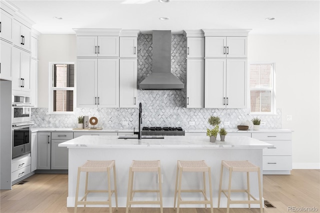 kitchen with backsplash, light wood-style flooring, a sink, and wall chimney exhaust hood