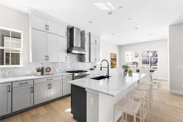 kitchen with a sink, light stone counters, tasteful backsplash, and wall chimney range hood