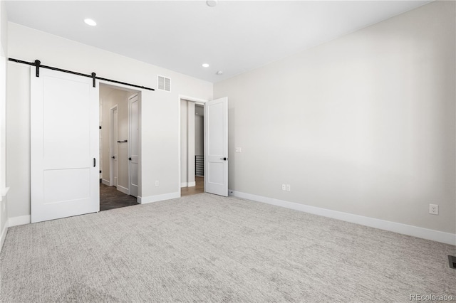 unfurnished bedroom featuring visible vents, a barn door, baseboards, and carpet floors