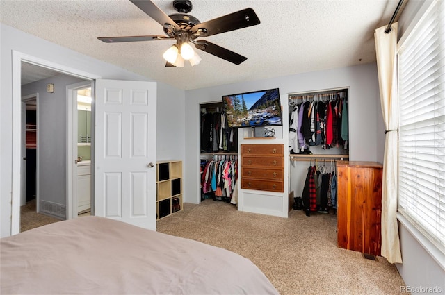 carpeted bedroom with multiple closets, ceiling fan, and a textured ceiling