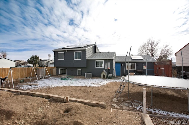 back of house with a playground, central AC unit, a trampoline, and solar panels