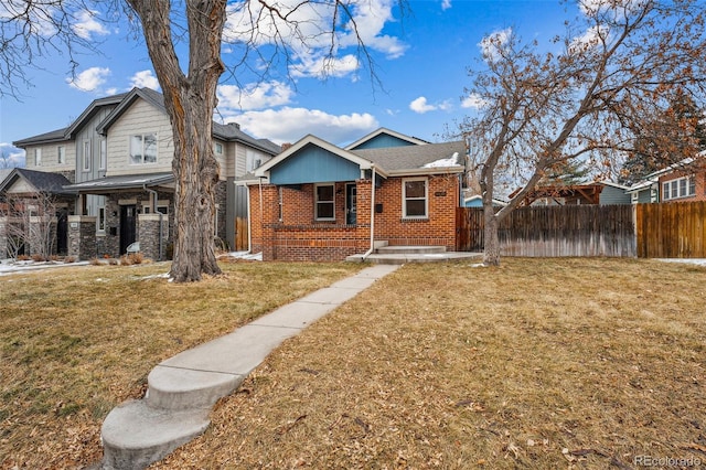 bungalow featuring a front yard, covered porch, brick siding, and fence