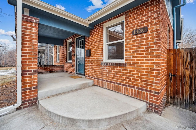 view of exterior entry with fence and brick siding