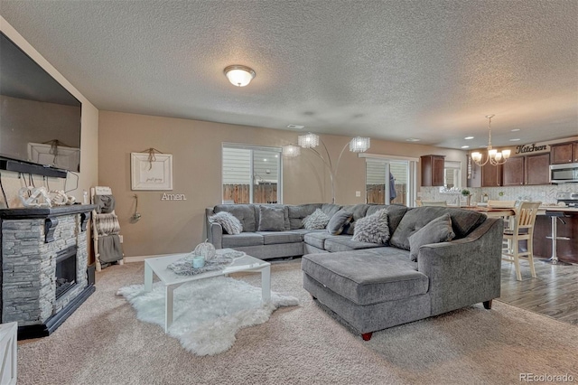 living area featuring a textured ceiling, an inviting chandelier, a fireplace, baseboards, and light colored carpet