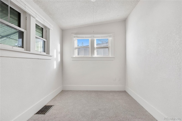 spare room with a textured ceiling, lofted ceiling, carpet floors, visible vents, and baseboards