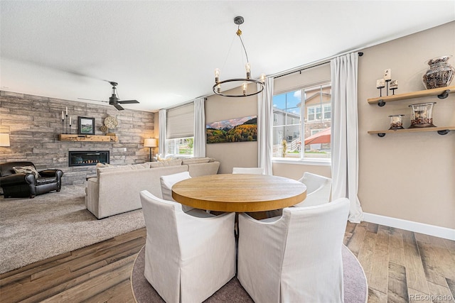 3480 Mount Powell Dr, Broomfield, CO 80023 - dining room featuring dark wood finished floors, a stone fireplace, a healthy amount of sunlight, and ceiling fan with notable chandelier