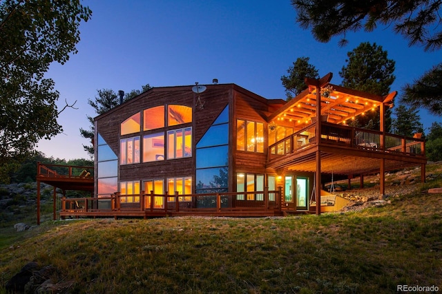 back house at dusk featuring a wooden deck, a yard, and a pergola