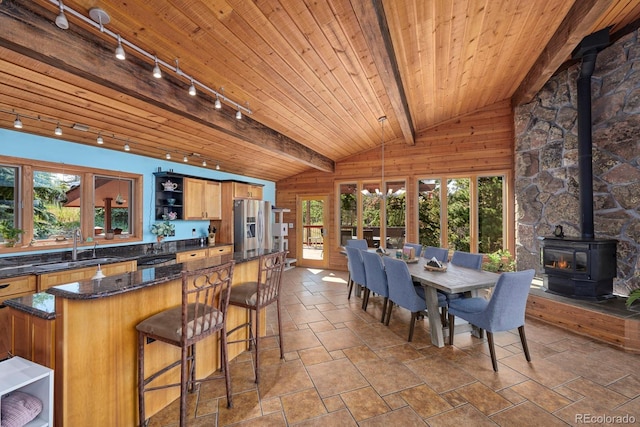 interior space with lofted ceiling with beams, wood ceiling, a wood stove, open shelves, and a sink