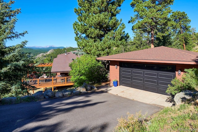 view of front of property with a deck with mountain view, a shingled roof, and an outdoor structure