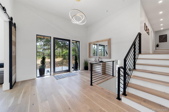 foyer entrance with an inviting chandelier, a towering ceiling, light hardwood / wood-style floors, and a barn door