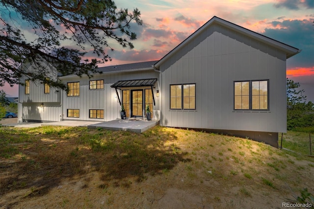 back house at dusk featuring a lawn and a patio