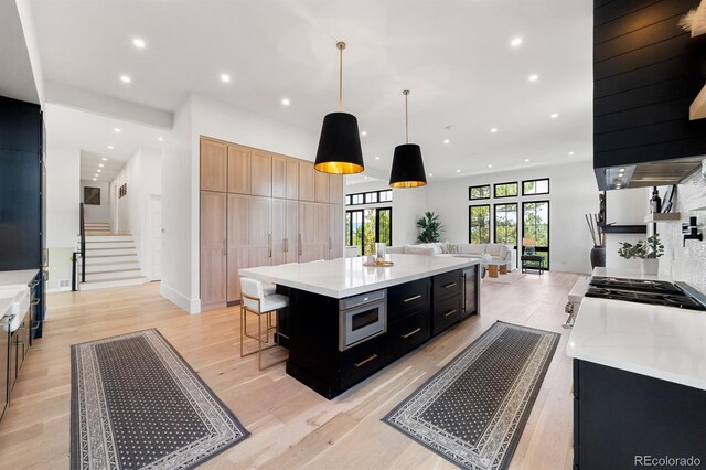 kitchen featuring light hardwood / wood-style flooring, a center island, stainless steel microwave, a kitchen bar, and decorative light fixtures