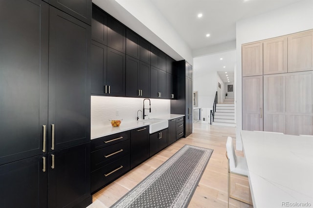 kitchen featuring tasteful backsplash, light stone countertops, sink, and light wood-type flooring