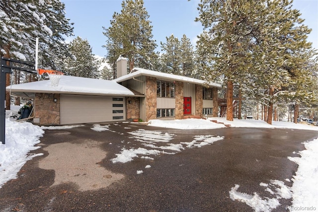 view of front facade featuring an attached garage, stone siding, driveway, and a chimney