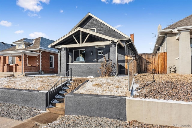 view of front of property with covered porch, brick siding, and fence