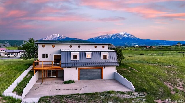 back house at dusk featuring a garage, a mountain view, and a lawn