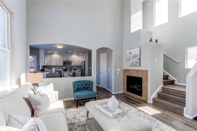 living room featuring a high ceiling, a tiled fireplace, and wood-type flooring