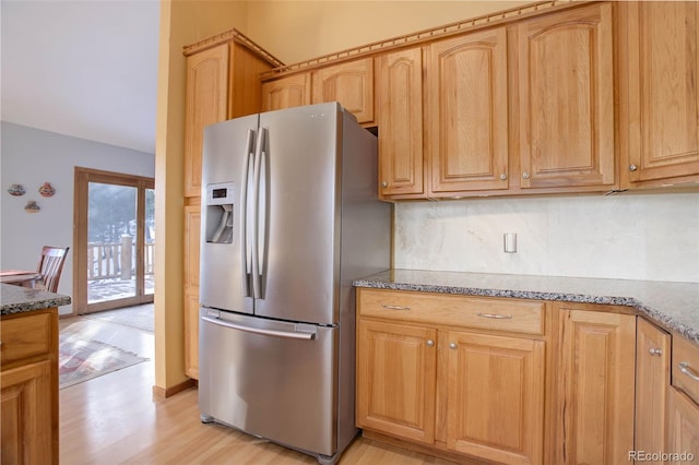 kitchen featuring stainless steel refrigerator with ice dispenser, tasteful backsplash, light hardwood / wood-style flooring, and dark stone countertops