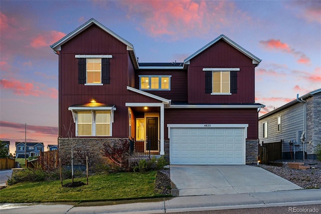 traditional-style house featuring a yard, fence, a garage, concrete driveway, and stone siding