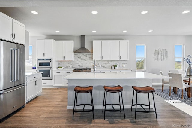 kitchen with a breakfast bar area, a sink, wall chimney range hood, appliances with stainless steel finishes, and tasteful backsplash