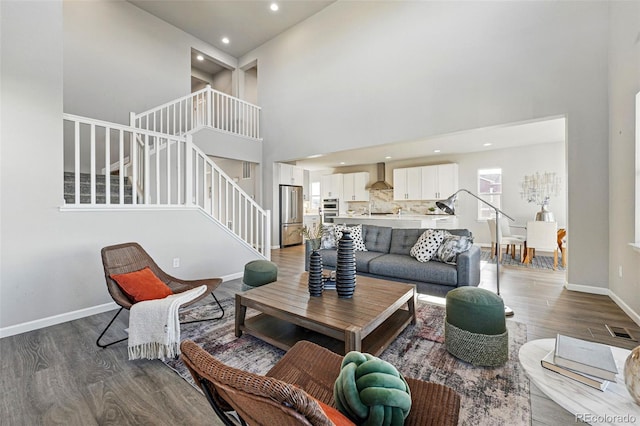 living area with stairs, wood finished floors, a towering ceiling, visible vents, and recessed lighting