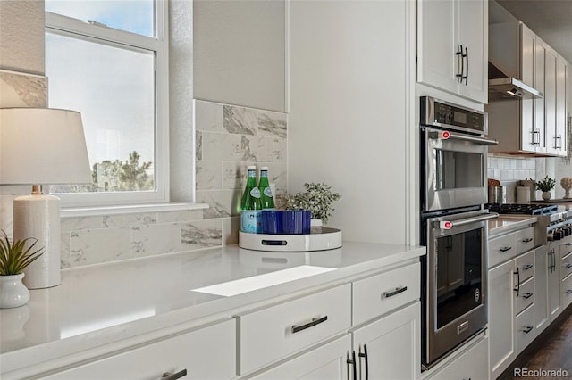 kitchen with stainless steel appliances, white cabinetry, exhaust hood, backsplash, and light countertops