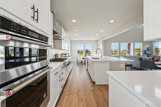 kitchen featuring a sink, wood finished floors, decorative backsplash, light countertops, and appliances with stainless steel finishes