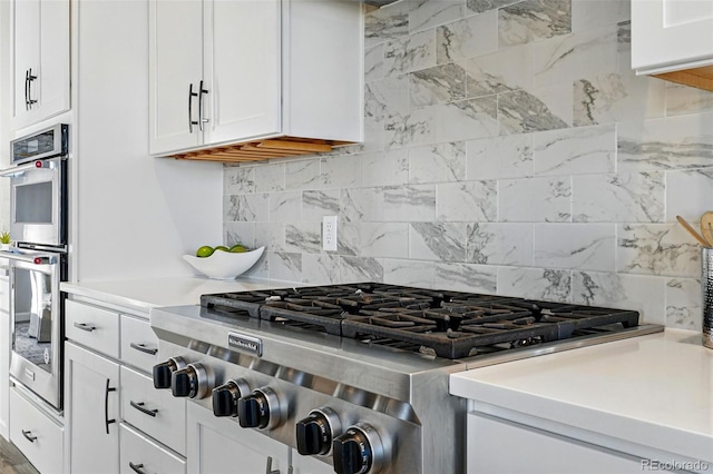 kitchen with stainless steel double oven, white cabinets, stove, backsplash, and light countertops