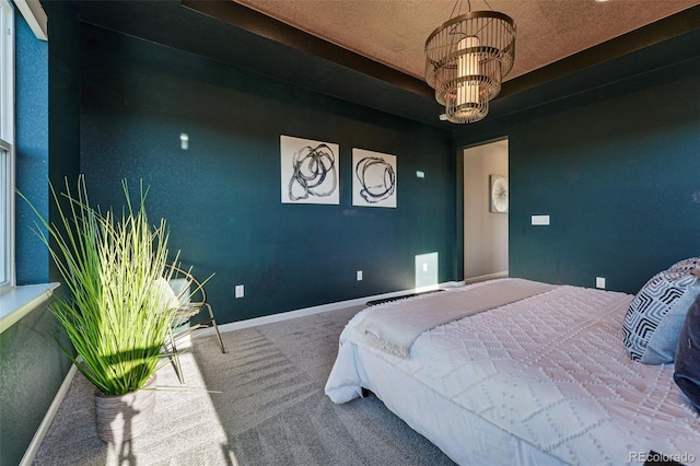 carpeted bedroom featuring a tray ceiling, a chandelier, and baseboards