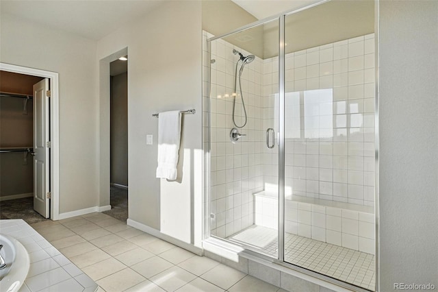 bathroom featuring a stall shower, a walk in closet, baseboards, and tile patterned flooring