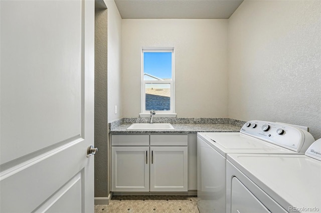 laundry area featuring cabinet space, washing machine and dryer, a textured wall, and a sink