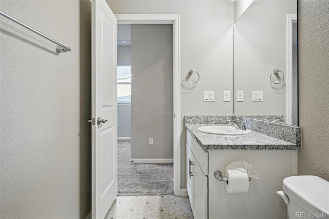 bathroom featuring vanity, toilet, a textured wall, and baseboards