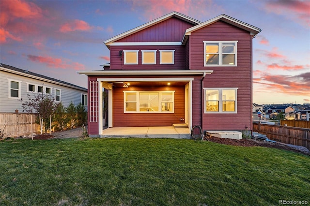 back of house at dusk featuring a yard, fence, and a patio