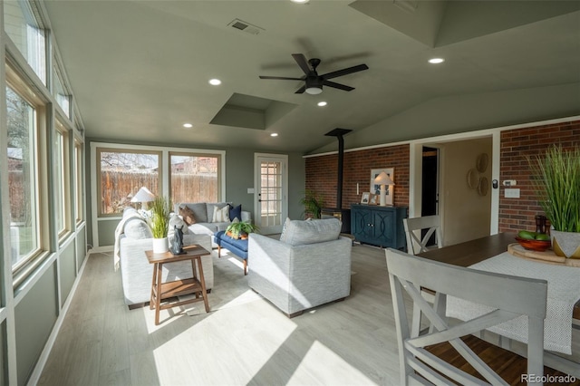 sunroom / solarium with visible vents, ceiling fan, vaulted ceiling, and a wood stove