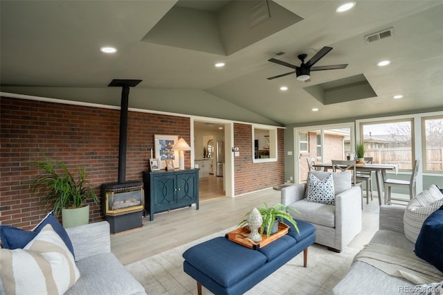 interior space featuring brick wall, visible vents, light wood-style floors, vaulted ceiling, and a wood stove