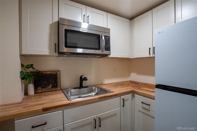 kitchen with butcher block countertops, a sink, appliances with stainless steel finishes, and white cabinets