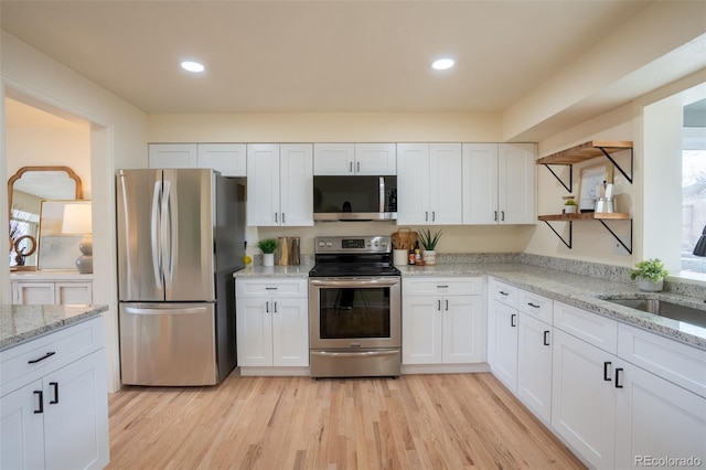 kitchen with light wood-type flooring, appliances with stainless steel finishes, white cabinets, and a sink