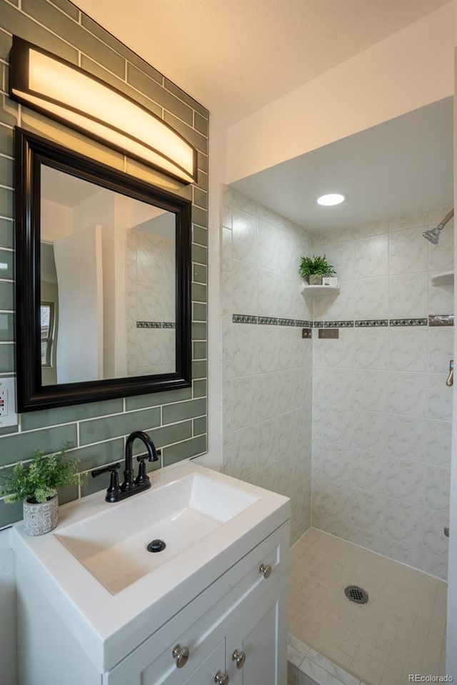 full bath featuring a tile shower, backsplash, vanity, and tile walls